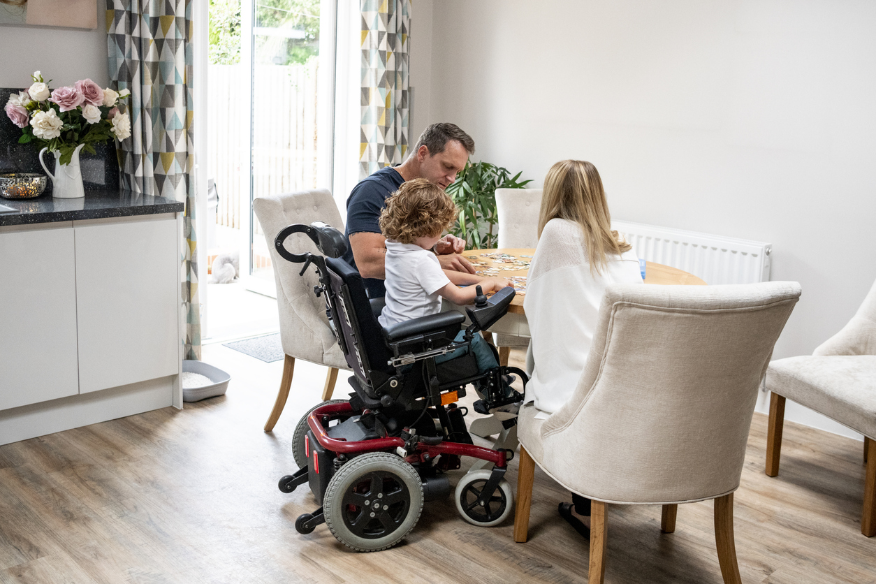 Boy in wheelchair doing jigsaw with parents Boy in wheelchair doing jigsaw with parents