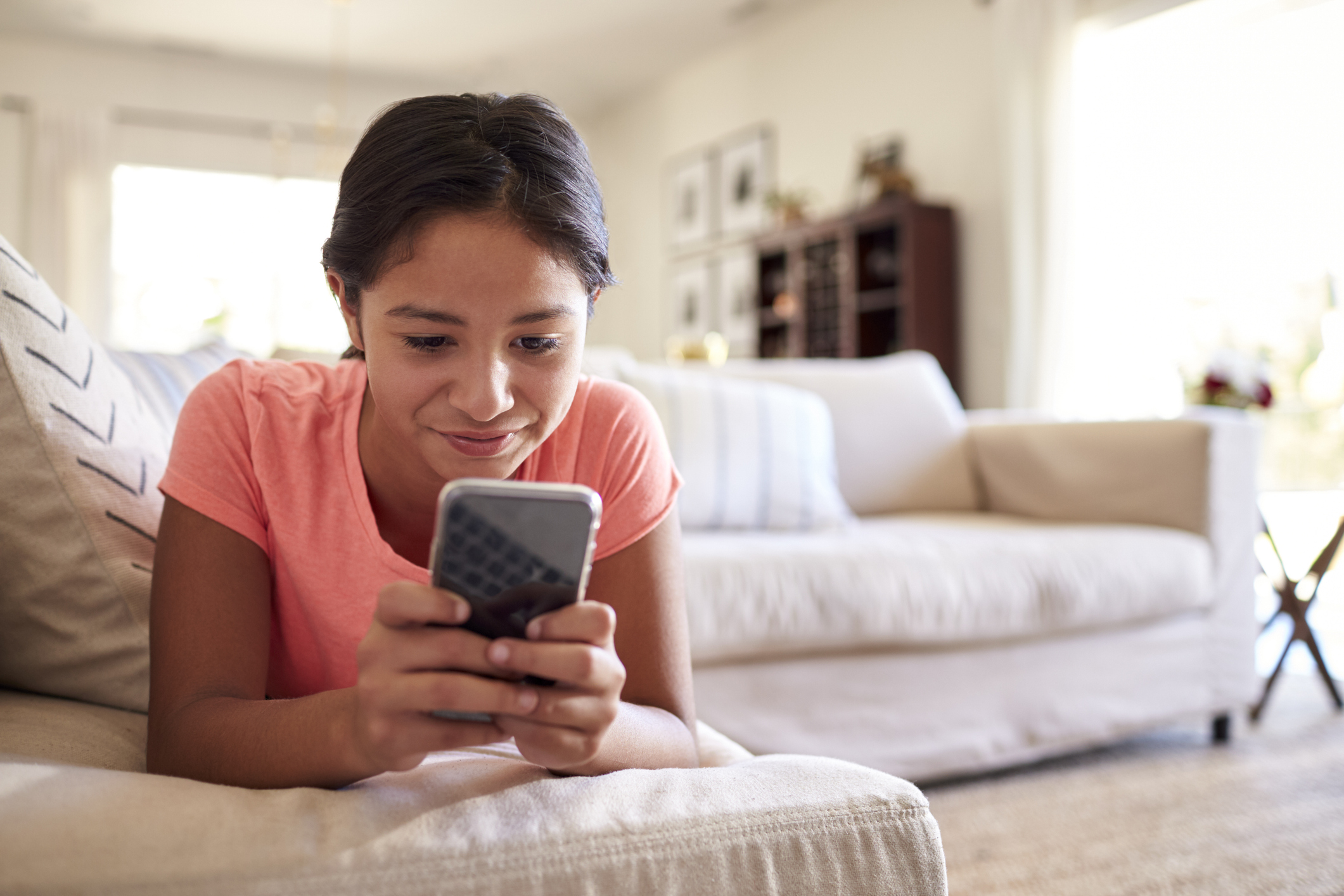 Teenage girl lying on the sofa at home in the living room using smartphone, close up, low angle, close up Teenage girl lying on the sofa at home in the living room using smartphone, close up, low angle, close up