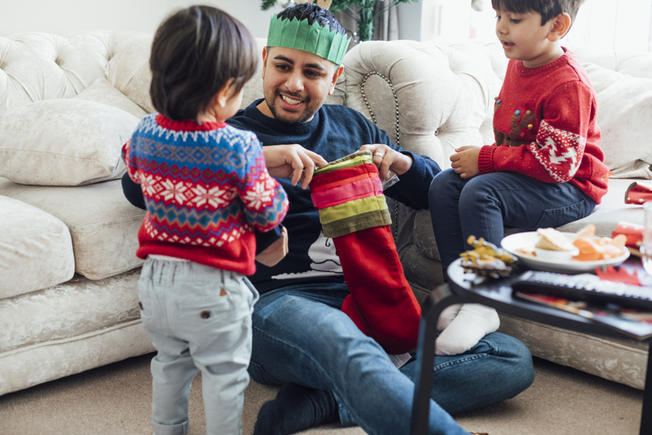 Opening Stockings A mid-adult man sitting with his two sons in the home living room during the Christmas period time. The father is opening a stocking while the children watch.