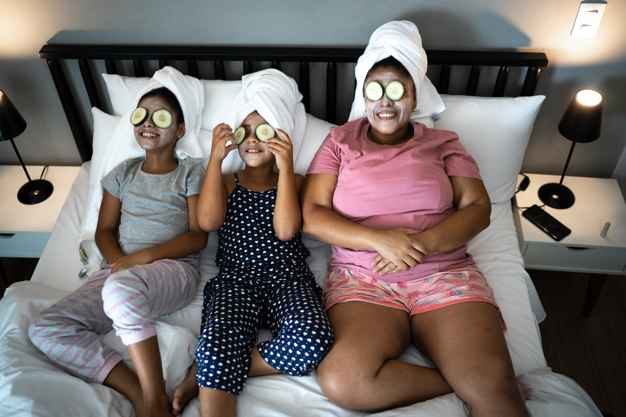 Morther and daughters in bed doing skin care with cucumber slices over the eyes Morther and daughters in bed doing skin care with cucumber slices over the eyes