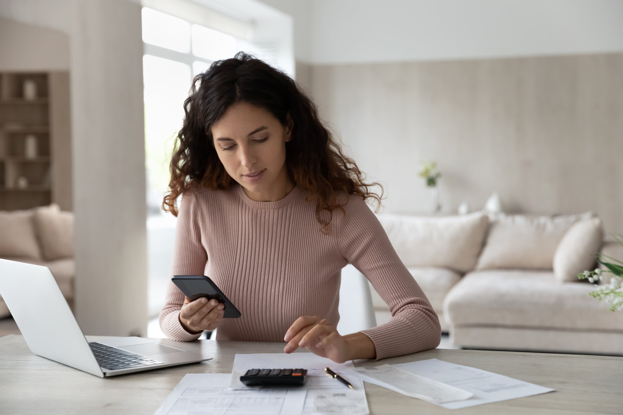 Latino woman pay bills on cell calculate on machine Latino woman pay bills on cell calculate on machine
