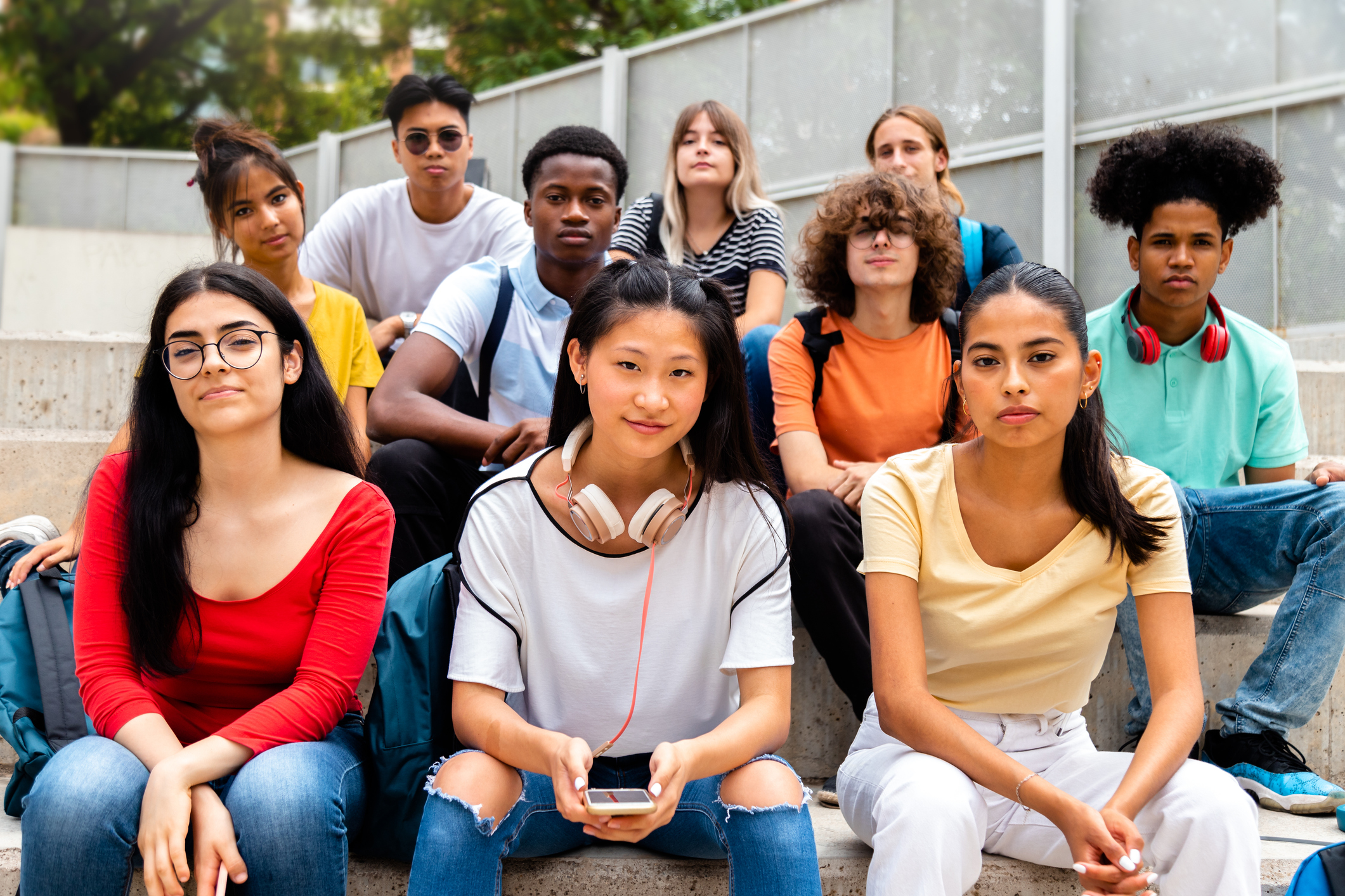 Group of multiracial teen high school students looking at camera sit on stairs outdoors. Group of multiracial teen high school students looking at camera sit on stairs outdoors.
