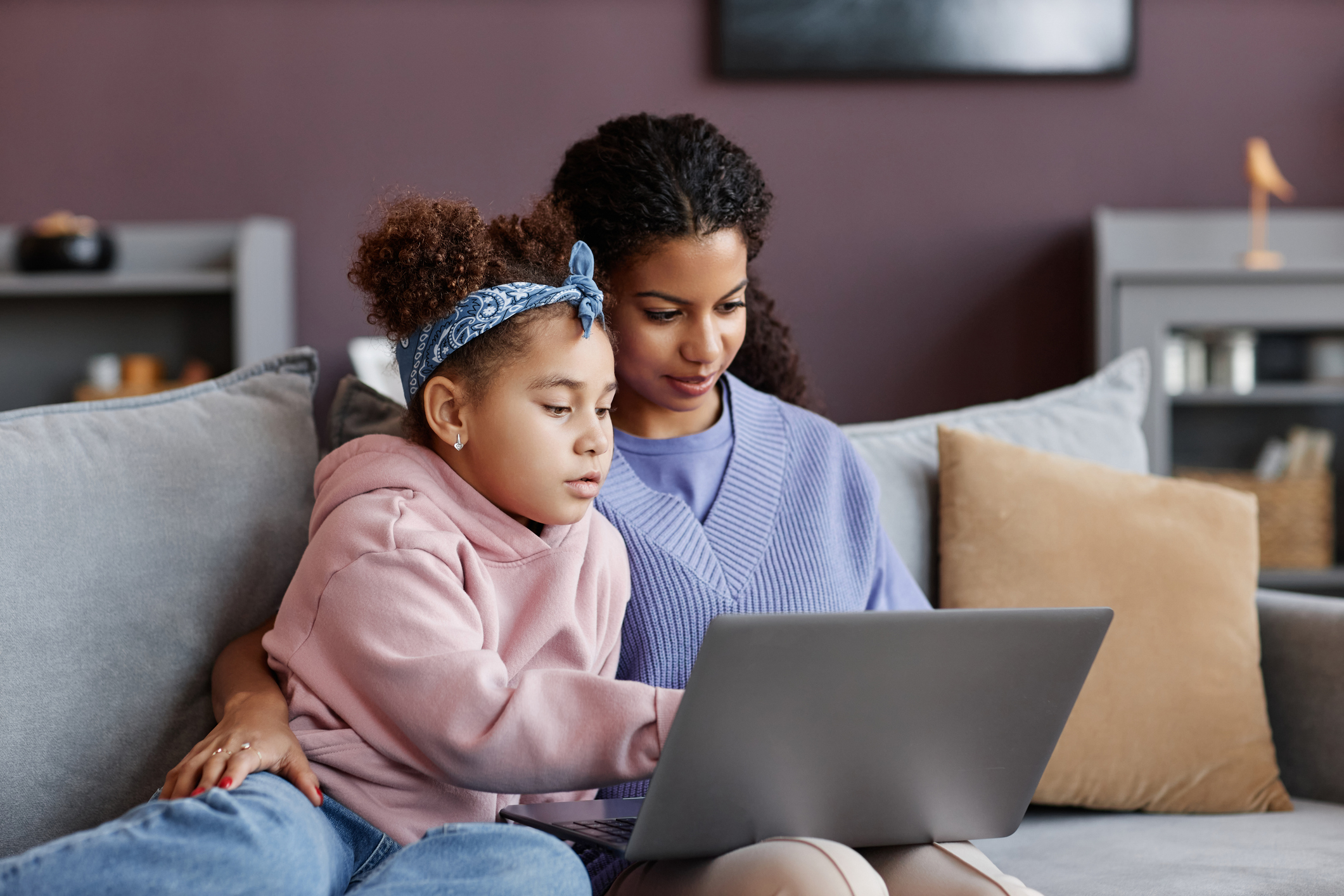 Black mother and daughter using laptop sitting on sofa together Black mother and daughter using laptop sitting on sofa together