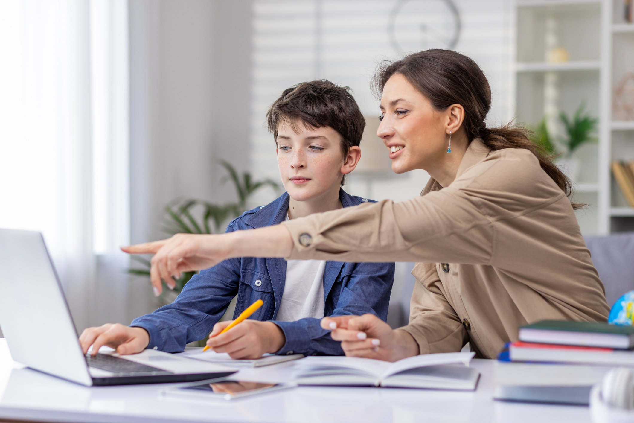 Mother and son studying together sitting at desk at home in living room, boy and woman tutor teaching at home, doing homework together homework