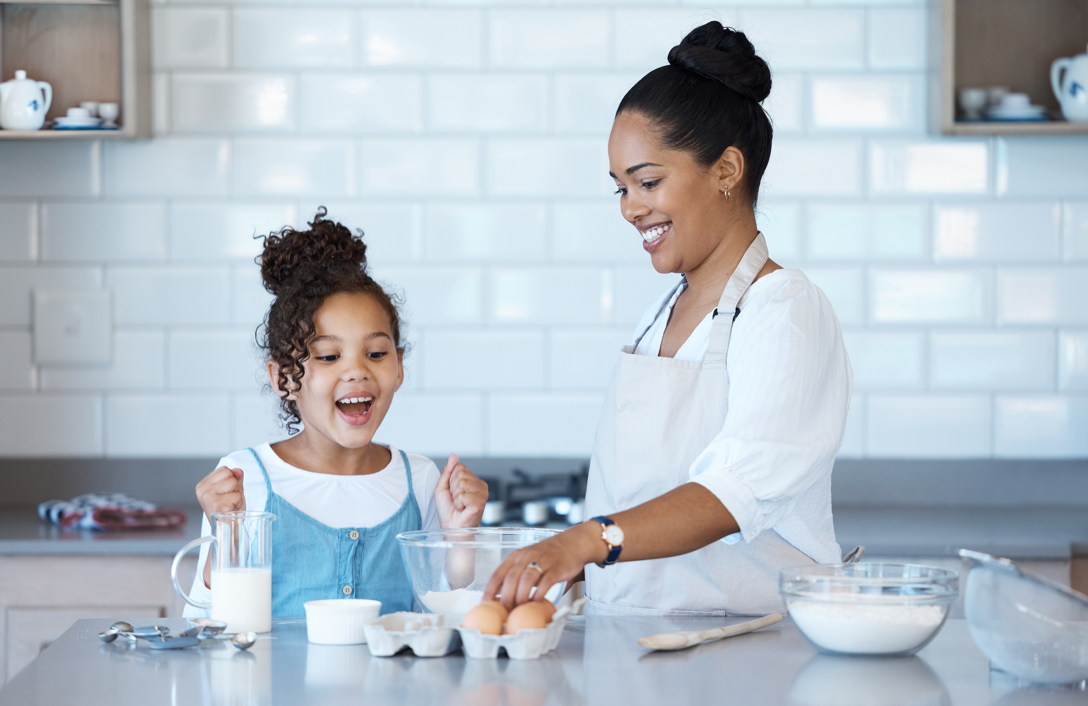 Happy young mixed race mother enjoying baking with her little daughter in the kitchen at home. Little hispanic girl smiling while helping her mother cook a meal at home Happy young mixed race mother enjoying baking with her little daughter in the kitchen at home. Little hispanic girl smiling while helping her mother cook a meal at home