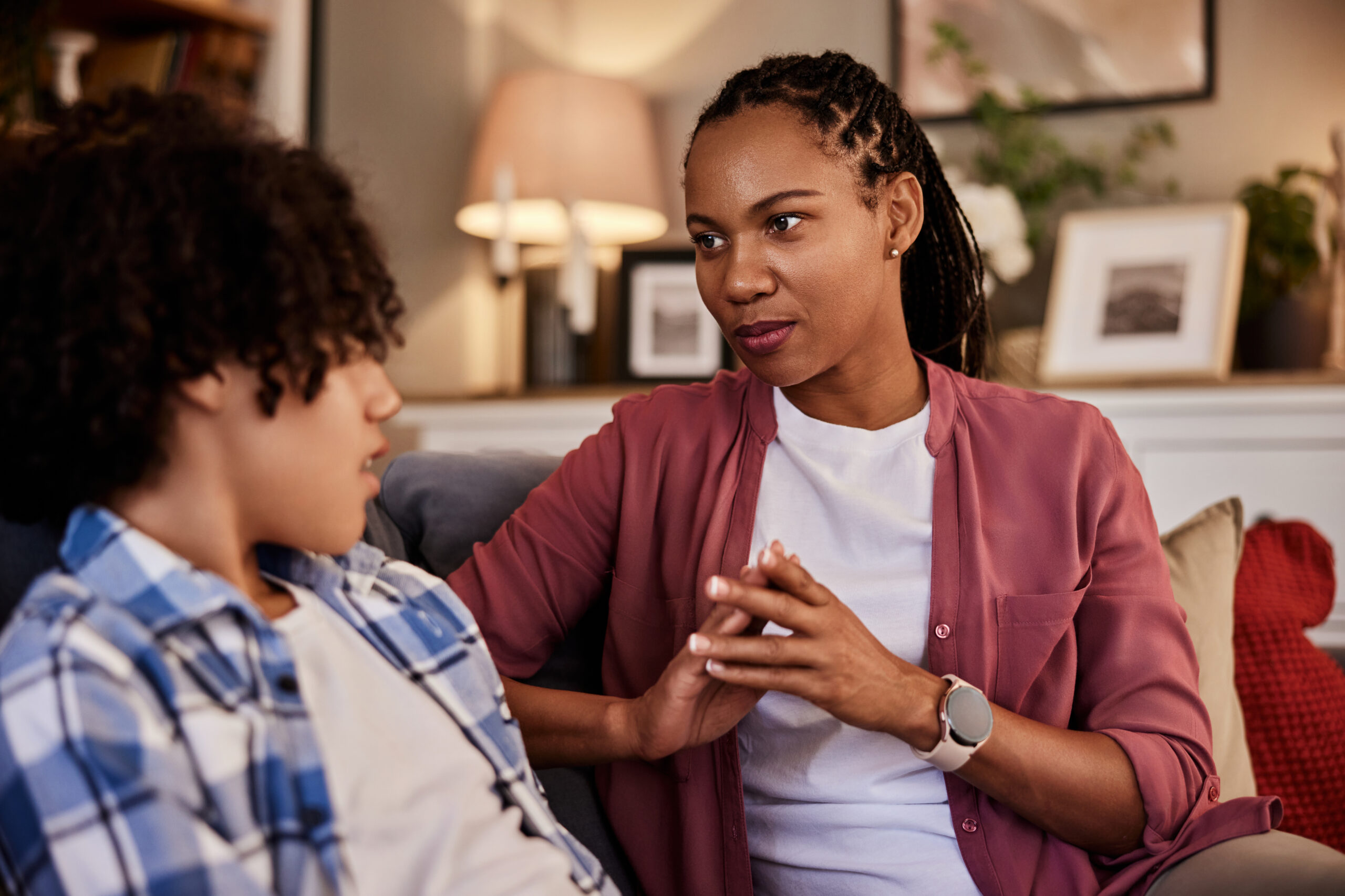 An African-American woman sitting on a couch with her teenage son and talking. An African-American woman sitting on a couch with her teenage son and talking.